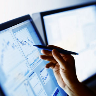 2台のモニターとペンでグラフを指す手