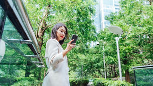 Low angle view of young Asian woman having a video call on smartphone, taking a break at city park.