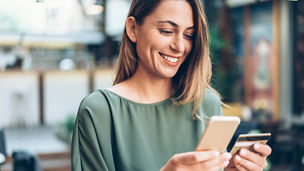Young woman shopping online in cafe using smartphone and credit card