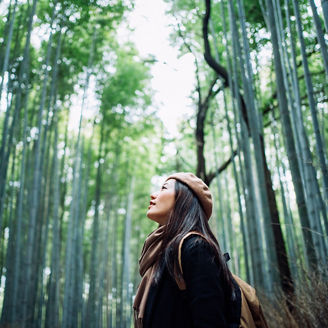 Young Asian female backpacker enjoying in nature. Taking a deep breath of fresh air while having a relaxing walk in the bamboo forest in the countryside during the outbreak of coronavirus pandemic