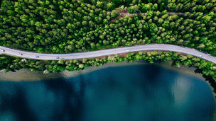 Aerial view of road between green summer forest and blue lake in Finland