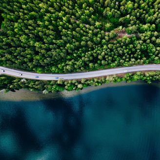 Aerial view of road between green summer forest and blue lake in Finland