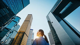 オフィスビル群の谷間をゆく一人の女性