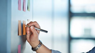 Japanese alt text: 壁に貼った付箋に書き込む人