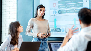 A software development team is engaged in brainstorming and idealization, leveraging flowchart data and software prototypes via a digital display to refine the design process and ensure it aligns with user needs within a technology startup office.