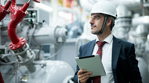 Mature Businessman with tablet in a factory boiler control room. Industrial boiler room ventilation.
