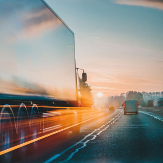 Japanese alt text: 夕闇の中道路を走るトラック