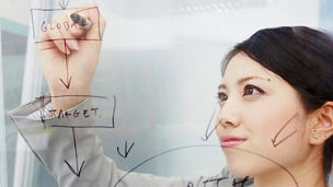 Japanese alt text: クリアボードに図を書くビジネスウーマン