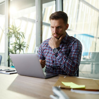 Young male entrepreneur brainstorming while reading an e-mail on a computer in the office.