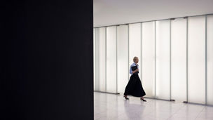 A smiling woman walking through a bright corridor, carrying a laptop