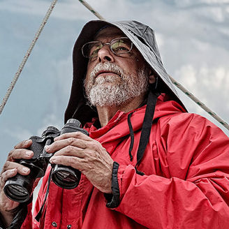 Kapitän in Regenklamotten hält ein Fernglas in der Hand