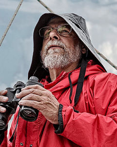 Kapitaen mit Regenkleidung hält Fernglas in der Hand
