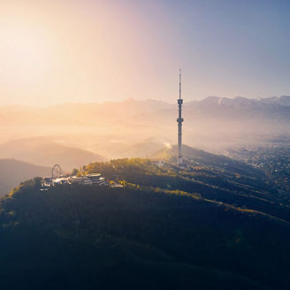 Aerial drone shot of symbol Almaty city high TV tower and park at Koktobe hill against snow mountains at sunrise in Kazakhstan