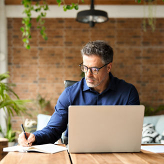 Busy mature middle aged professional businessman executive using laptop at work writing notes. 50 years old business man company manager investor working on computer technology sitting at office desk.