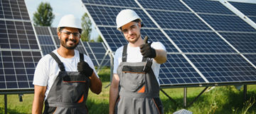 Two skilled workers or craftsmen wearing working gray uniforms, technicians are installing solar panels on a solar farm for clean energy and electricity supply.