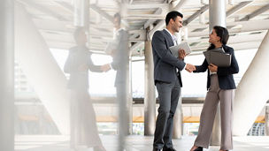 Indian businessman greeting and making handshake with a businesswoman outdoors in city walkway