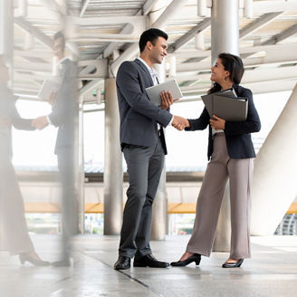 Indian businessman greeting and making handshake with a businesswoman outdoors in city walkway