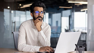 Portrait of a thoughtful and serious Indian male businessman sitting in the office at the workplace and working on a laptop.