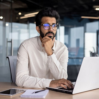 Portrait of a thoughtful and serious Indian male businessman sitting in the office at the workplace and working on a laptop.