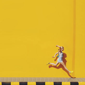 Frau springt vor gelber Wand