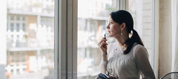 Person står og snakker i mikron på mobilen ved et stor vindu på et kontor 