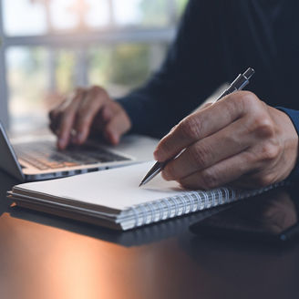 E-learning, online study, learn from home, teleworking concept. Close up, business man hand with pen writing on notebook, working with laptop computer on desk at home office. Student studying online, lecturing on notepad, close up