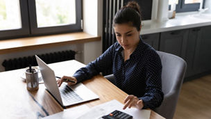 Bookkeeping. Busy millennial indian woman professional accountant preparing annual financial report checking result on calculator. Mixed race female freelancer counting tax rates declaring income