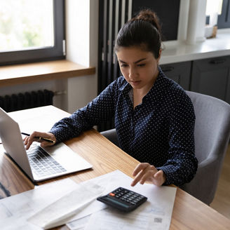 Bookkeeping. Busy millennial indian woman professional accountant preparing annual financial report checking result on calculator. Mixed race female freelancer counting tax rates declaring income