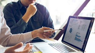 Two businessmen are together analyzing the financial data graph and pointing to the laptop computer screen.