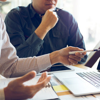 Two businessmen are together analyzing the financial data graph and pointing to the laptop computer screen.