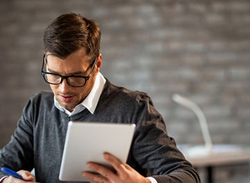 Male entrepreneur taking notes while going through paperwork and using touchpad at work. 