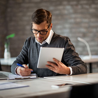 Male entrepreneur taking notes while going through paperwork and using touchpad at work. 