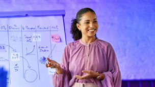 Mulher a apresentar uma ideia enquanto atrás é visível um quadro com dados escritos