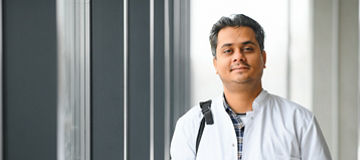 Portrait of a young Indian male medical student in a white coat waving.