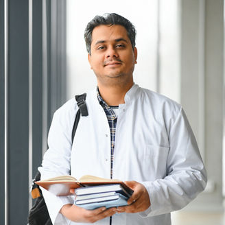 Portrait of a young Indian male medical student in a white coat waving.