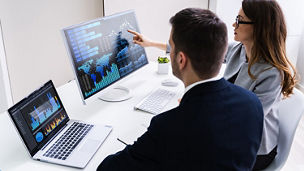 Homem e mulher a visualizar dados em dois computadores