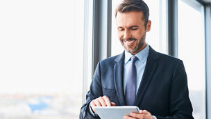 Happy businessman using digital tablet standing in office