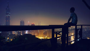 Man sitting on balcony railing looking at city view, 683777431