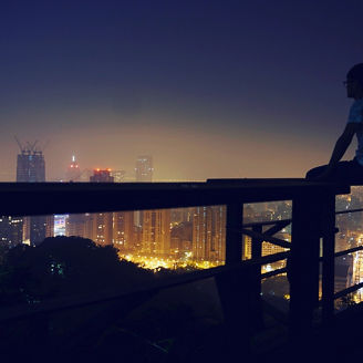 Man sitting on balcony railing looking at city view, 683777431