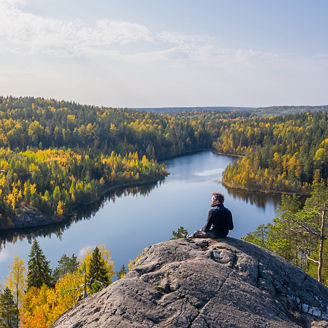 The man on top of a rock in the autumn forest on a background of a beautiful lake.