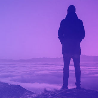 Man standing on mountain peak watching sunset