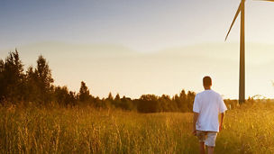 Person walking through a field with a wind turbine in the distance