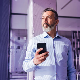 Homem com um telmóvel pensativo a olhar para uma janela enquanto o sol ilumina a sua cara