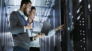 Male IT Specialist Holds Laptop and Discusses Work with Female Server Technician. They're Standing in Data Center, Rack Server Cabinet is Open.
