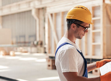 Construction worker wearing a hard hat reviewing plans inside an industrial or building site.