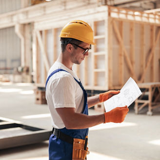 Construction worker wearing a hard hat reviewing plans inside an industrial or building site.