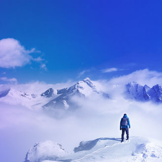 Person steht auf einem Berg umgeben von Wolken