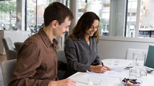 Man looking at woman smiling while signing agreement at desk in real estate office