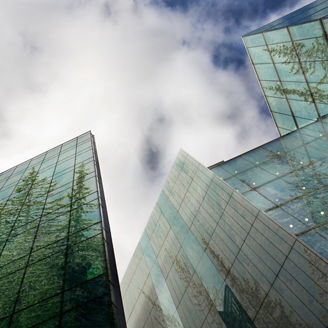 Modern glass office buildings reflecting trees under a cloudy sky.