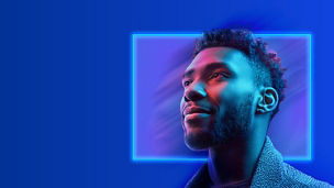 A close up shot of a person looking ahead whilst smiling. A light blue rectangle on a dark blue background sits behind them